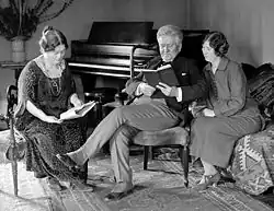 La Follette sitting down with his wife and daughter and reading a book